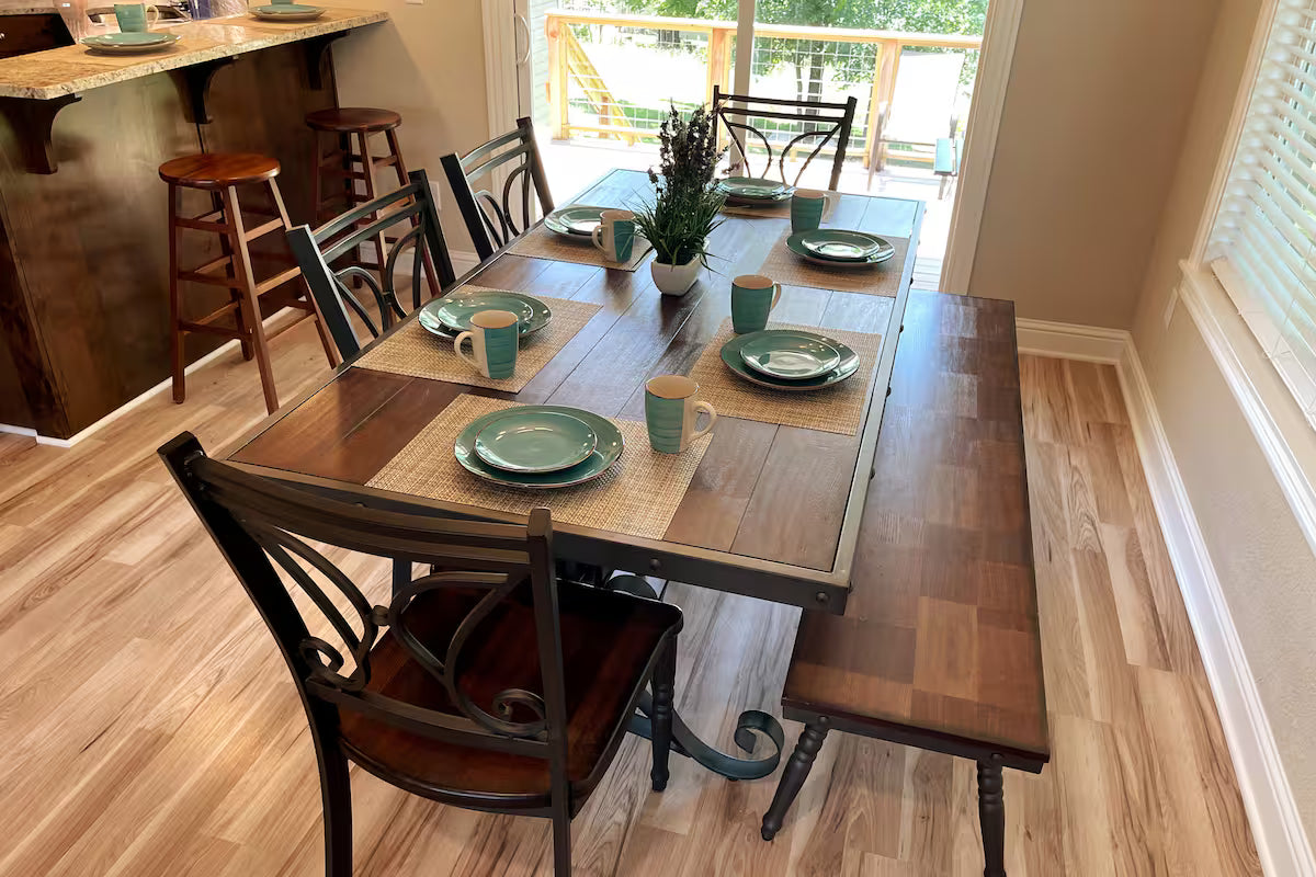 Dining room with a wooden table set for four, featuring green plates and mugs.