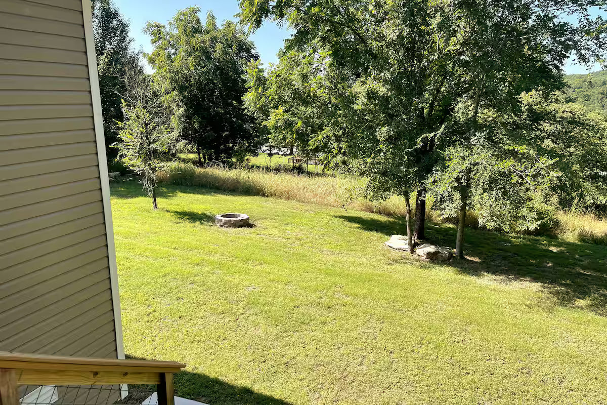 Backyard with grass, trees, and a fire pit on a sunny day in Woodland Retreat, Holiday Island