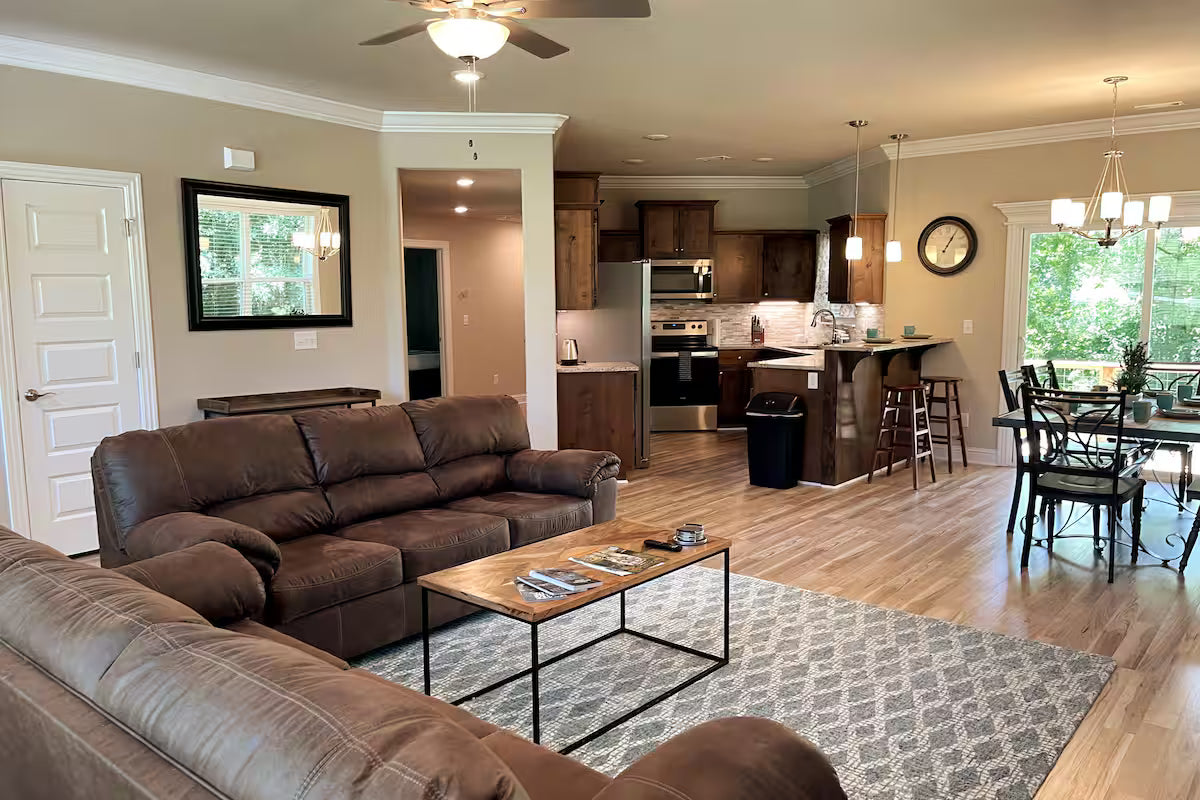 Living room with brown sofa, coffee table, and kitchen in the background